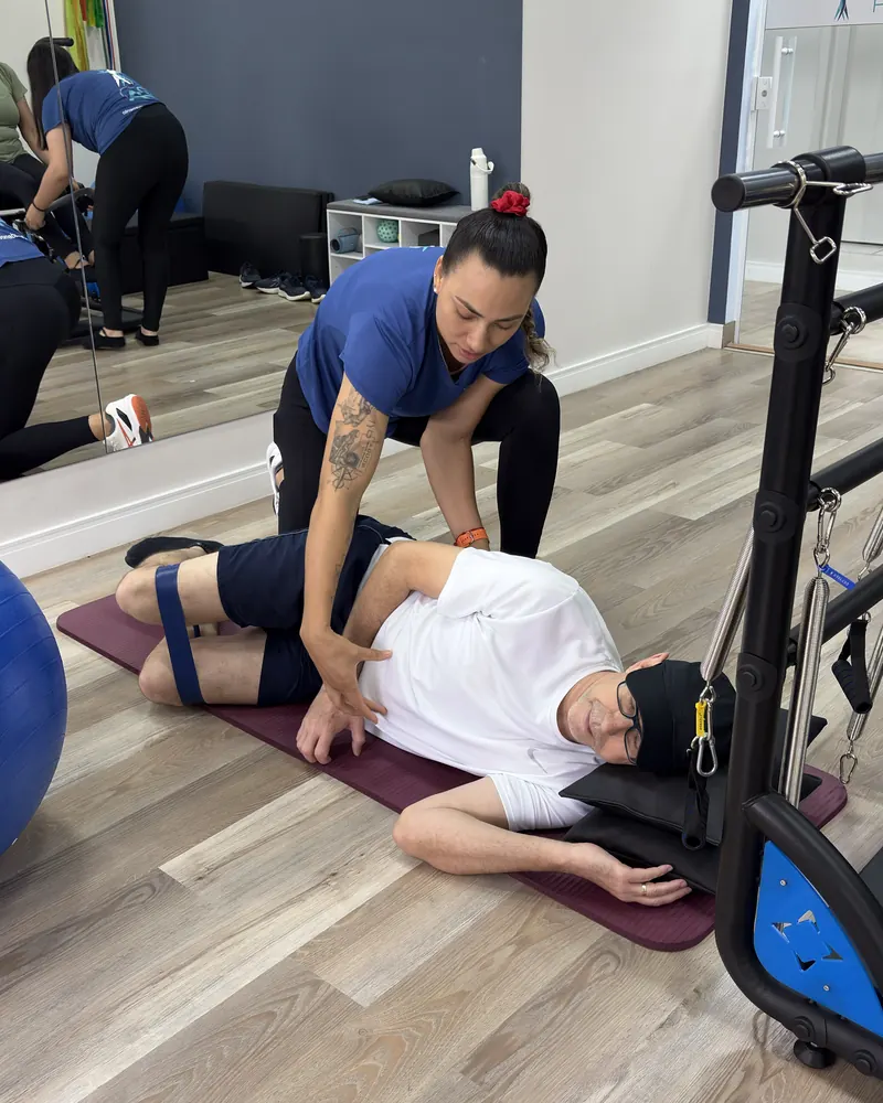 Professora orienta um aluno no colchonete durante um exercício com elástico